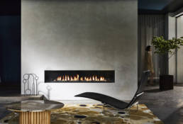 Fireplace built in the wall which has a grey background with the mustard rug on the floor along side a black resting chair
