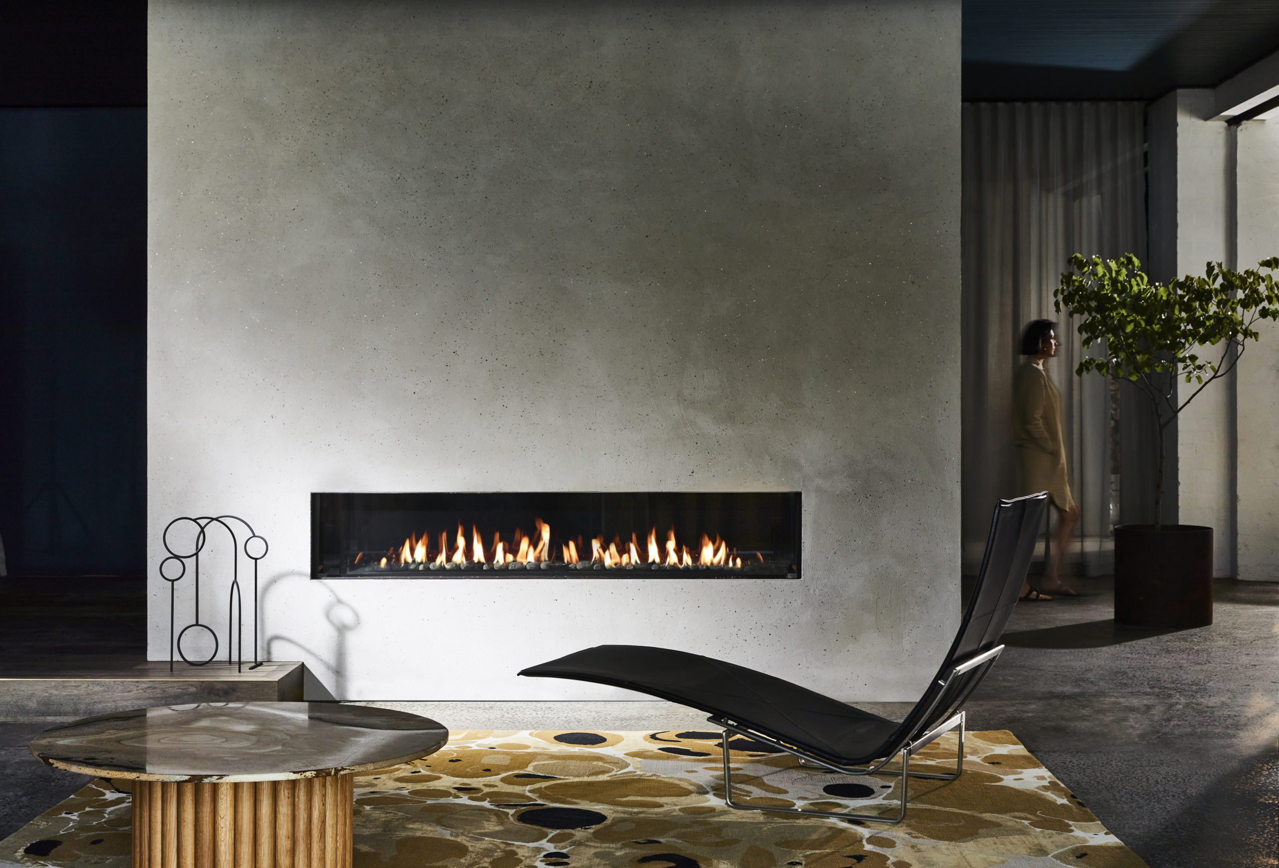 Fireplace built in the wall which has a grey background with the mustard rug on the floor along side a black resting chair